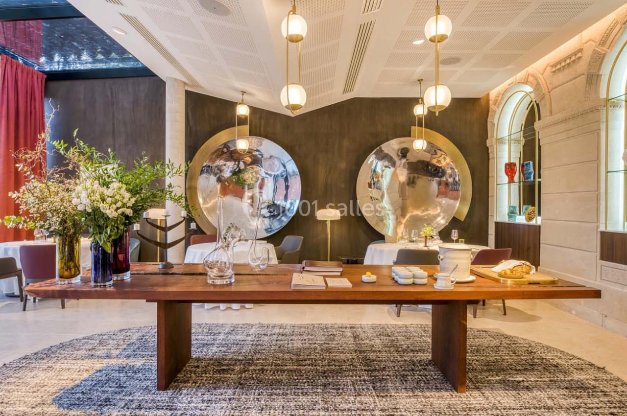 Table en bois avec objets décoratifs, entourée de luminaires suspendus et de miroirs ronds dans une salle élégante.