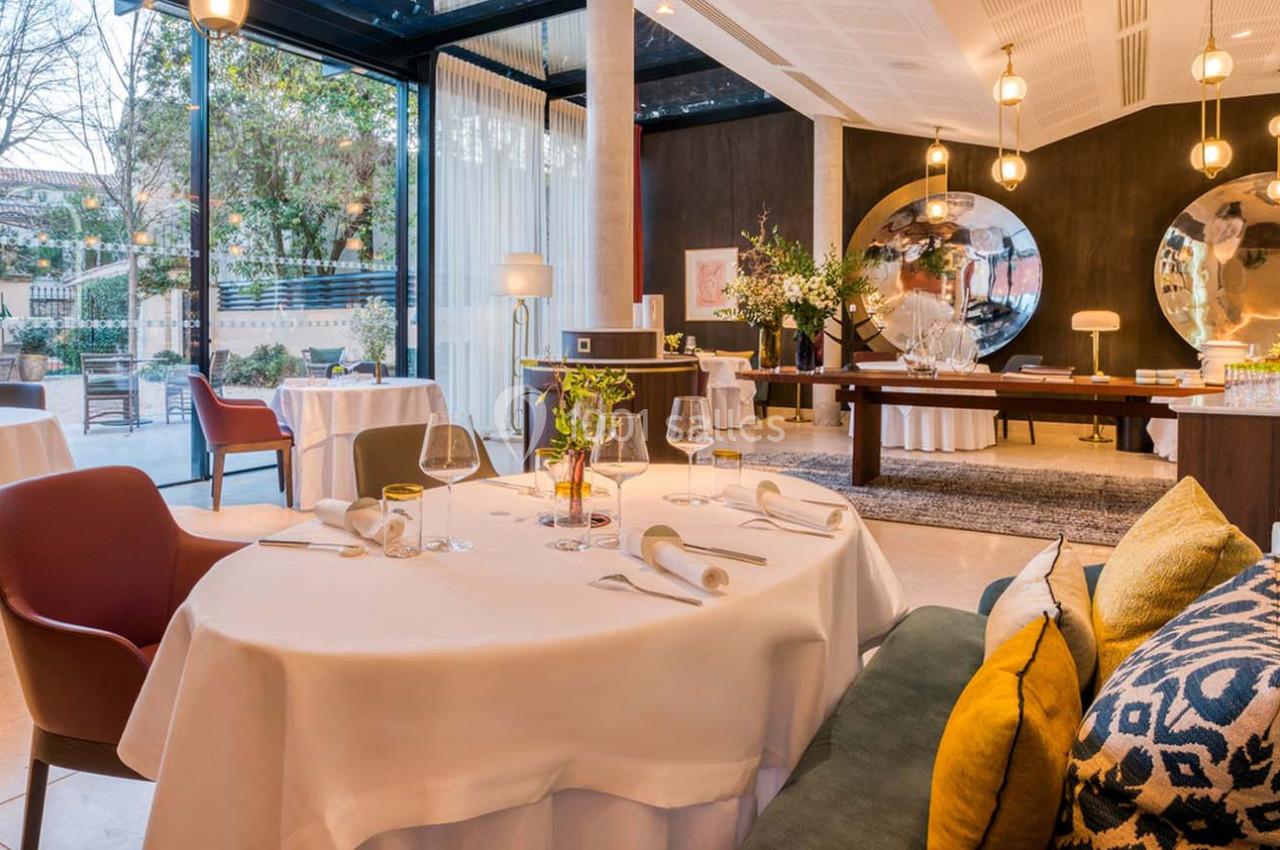 Salle de restaurant élégante avec tables dressées, grandes baies vitrées, miroirs ronds et décoration soignée.
