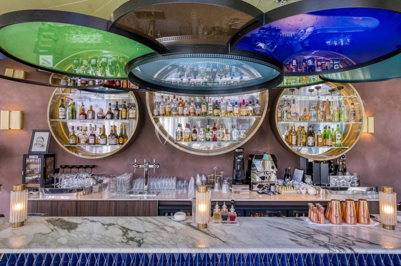 Bar moderne avec comptoir en marbre, étagères circulaires illuminées contenant des bouteilles d'alcool et des verres.