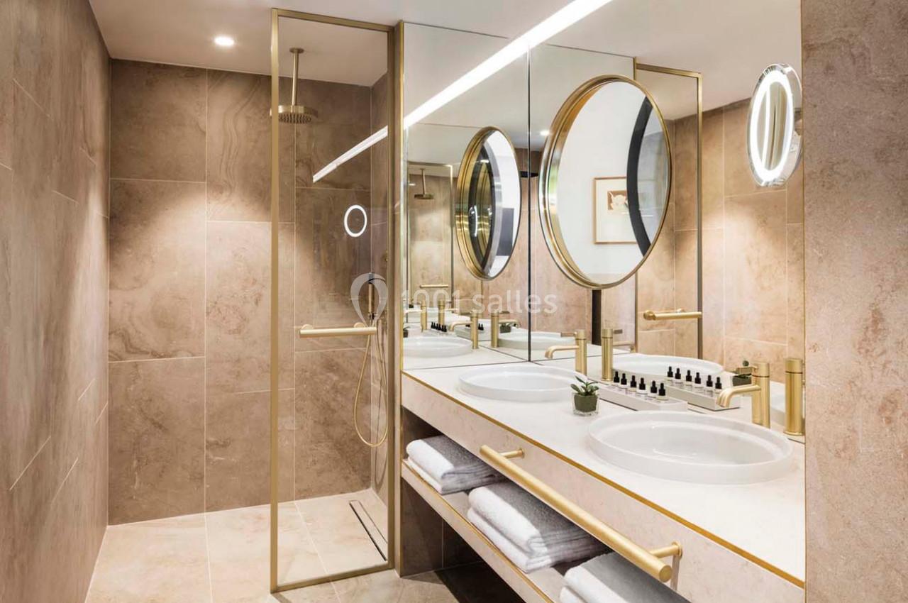 Salle de bain moderne avec double vasque, miroirs ronds, douche à paroi vitrée et finitions dorées.