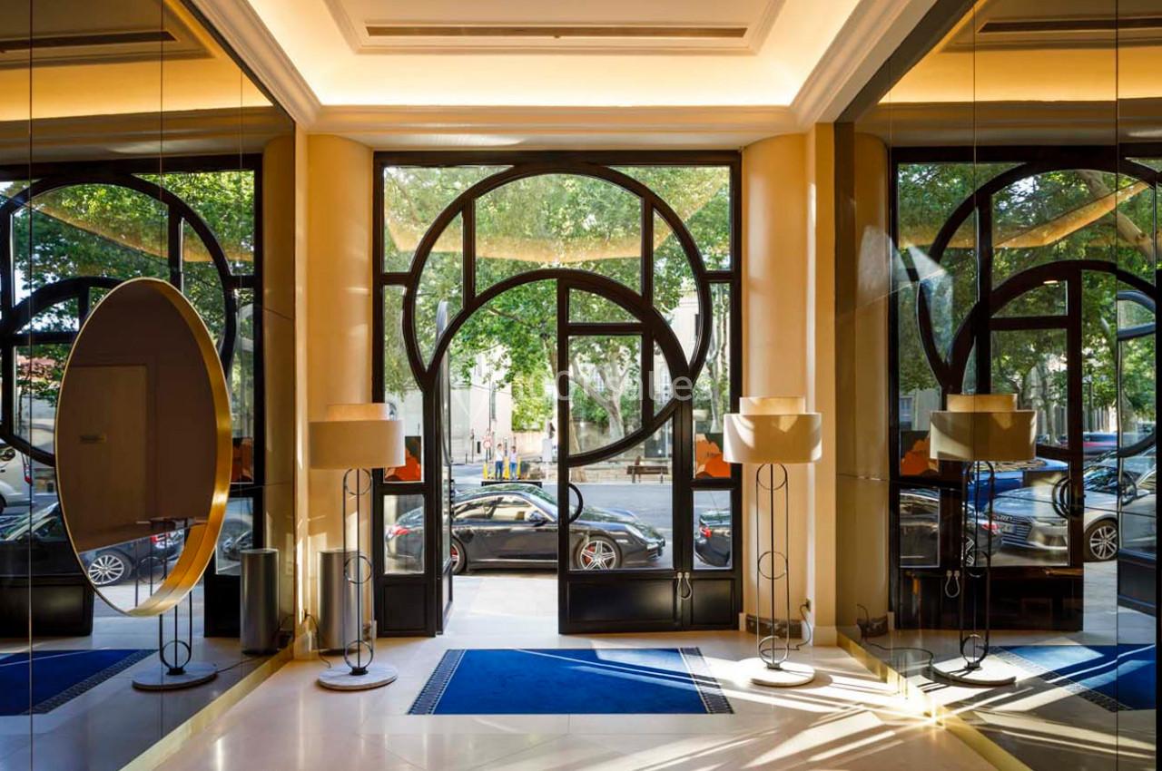 Entrée d'un bâtiment avec des portes vitrées, des miroirs, des lampes et une vue sur des arbres et des voitures à l…