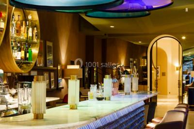 Piscine intérieure avec chaises longues rayées, éclairage doux et grande fenêtre ronde donnant sur l'extérieur.