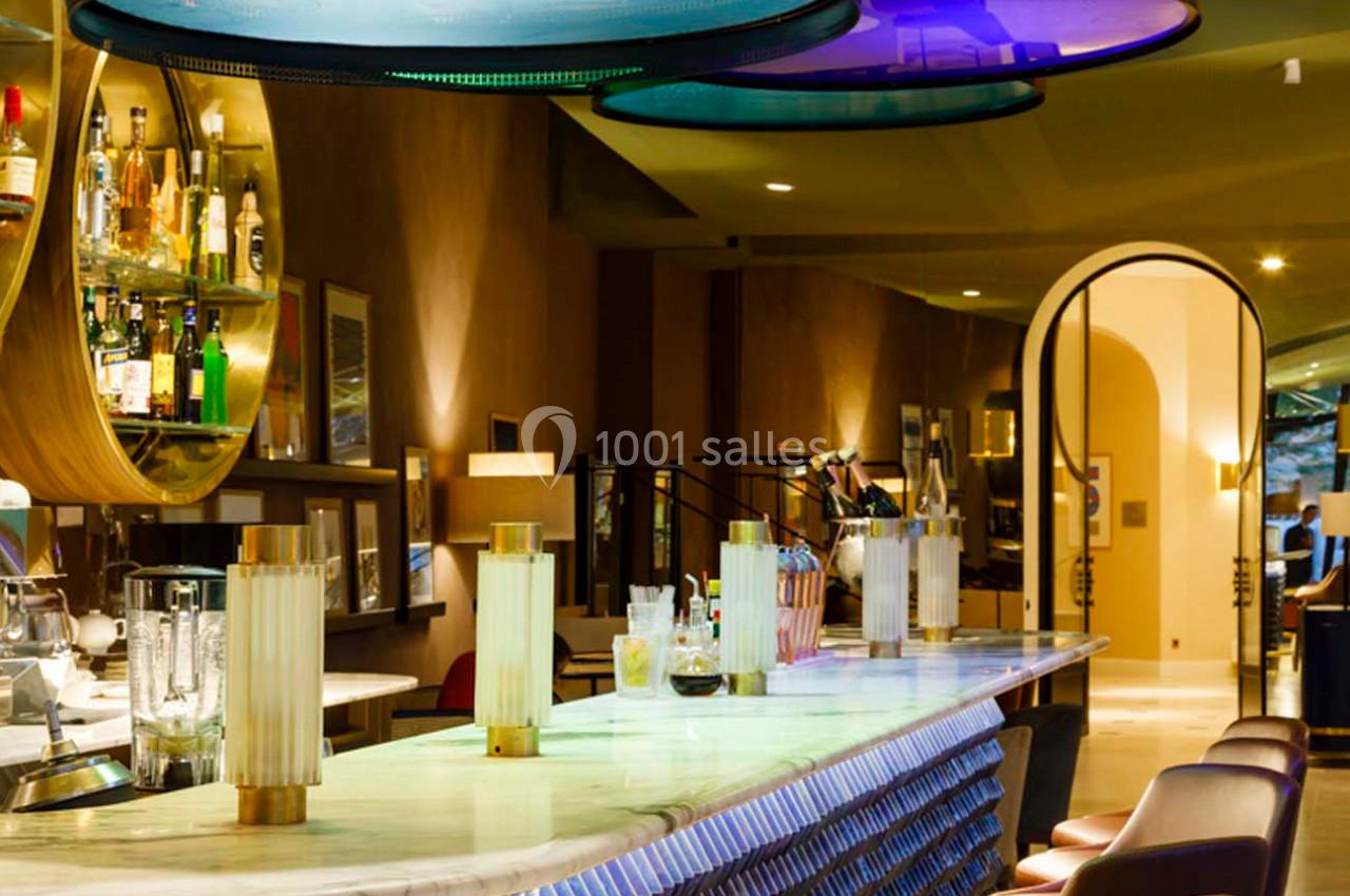 Bar élégant avec comptoir en marbre, tabourets alignés, étagères de bouteilles et éclairage moderne coloré.