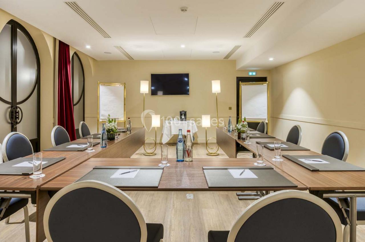 Salle de réunion lumineuse avec table en U, chaises noires, écrans, blocs-notes et bouteilles d'eau.