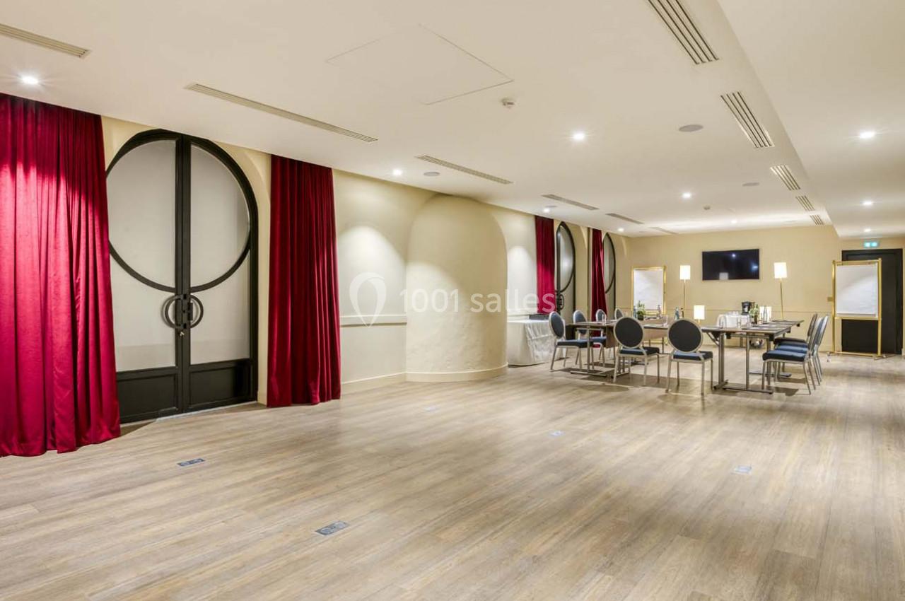 Salle de réunion lumineuse avec parquet, rideaux rouges, chaises et table équipée pour une réunion.