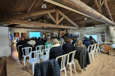 Salle avec des participants assis face à une présentation, entourée de drapeaux publicitaires et d'éléments décoratifs.