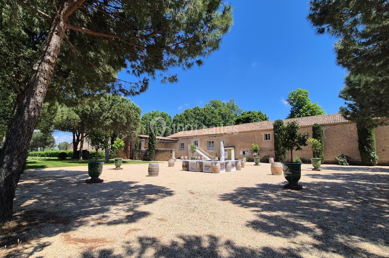 Cour ensoleillée avec fontaine centrale, entourée d'arbres, de pots décoratifs et d'un bâtiment en pierre.