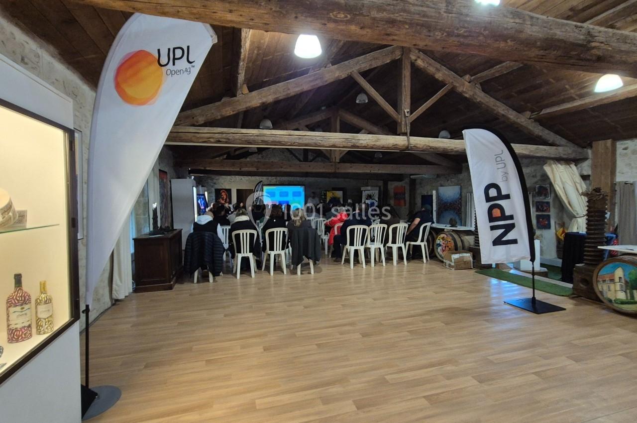 Salle avec des participants assis face à une présentation, entourée de drapeaux publicitaires et d'éléments décoratifs.