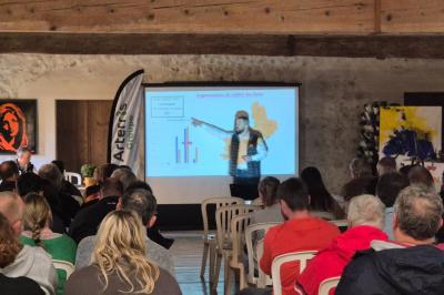 Salle avec des participants assis face à une présentation, entourée de drapeaux publicitaires et d'éléments décoratifs.