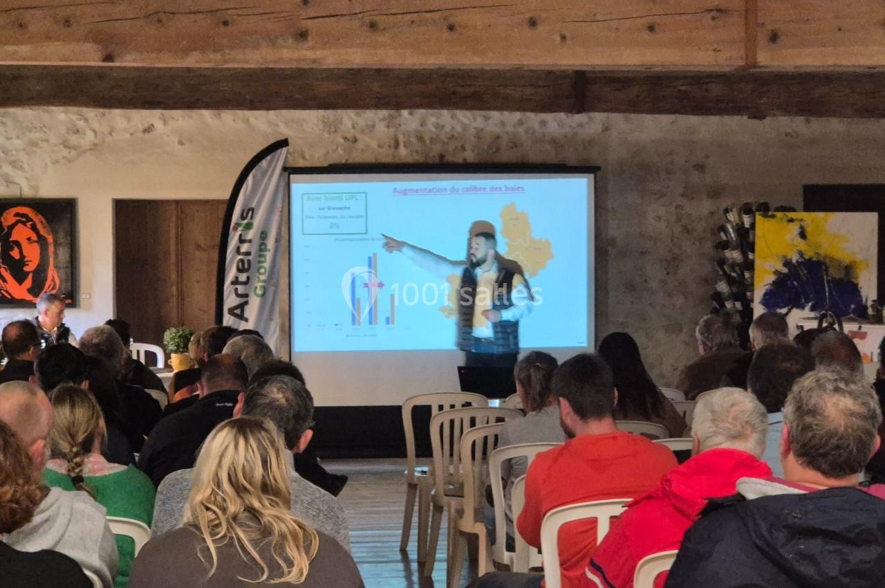 Une conférencière présente des graphiques sur un écran devant un public assis dans une salle en pierre.