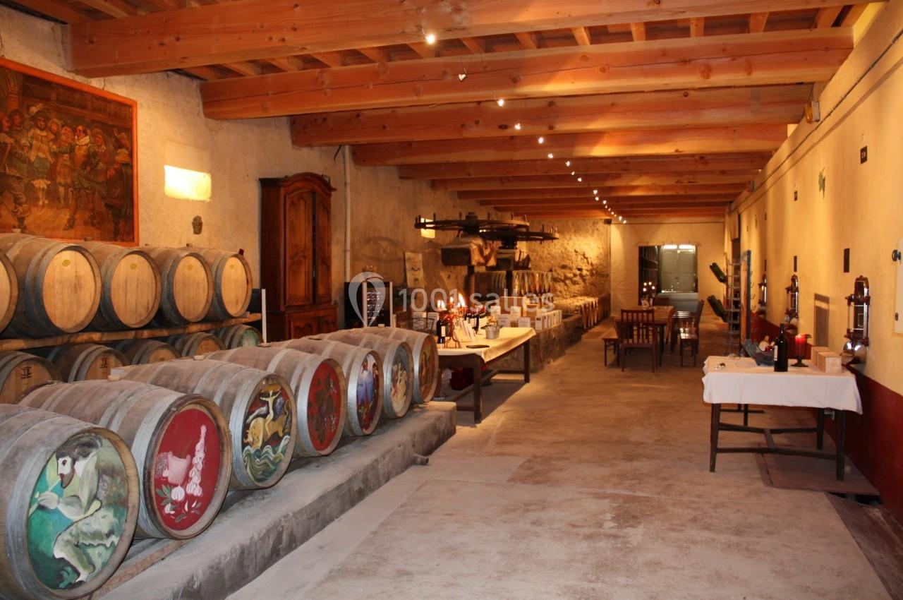 Salle de dégustation avec des tonneaux décorés, tables dressées et plafond en bois dans une cave viticole.