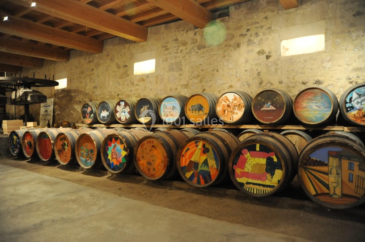 Rangée de tonneaux en bois décorés avec des peintures colorées, alignés dans une cave en pierre éclairée.