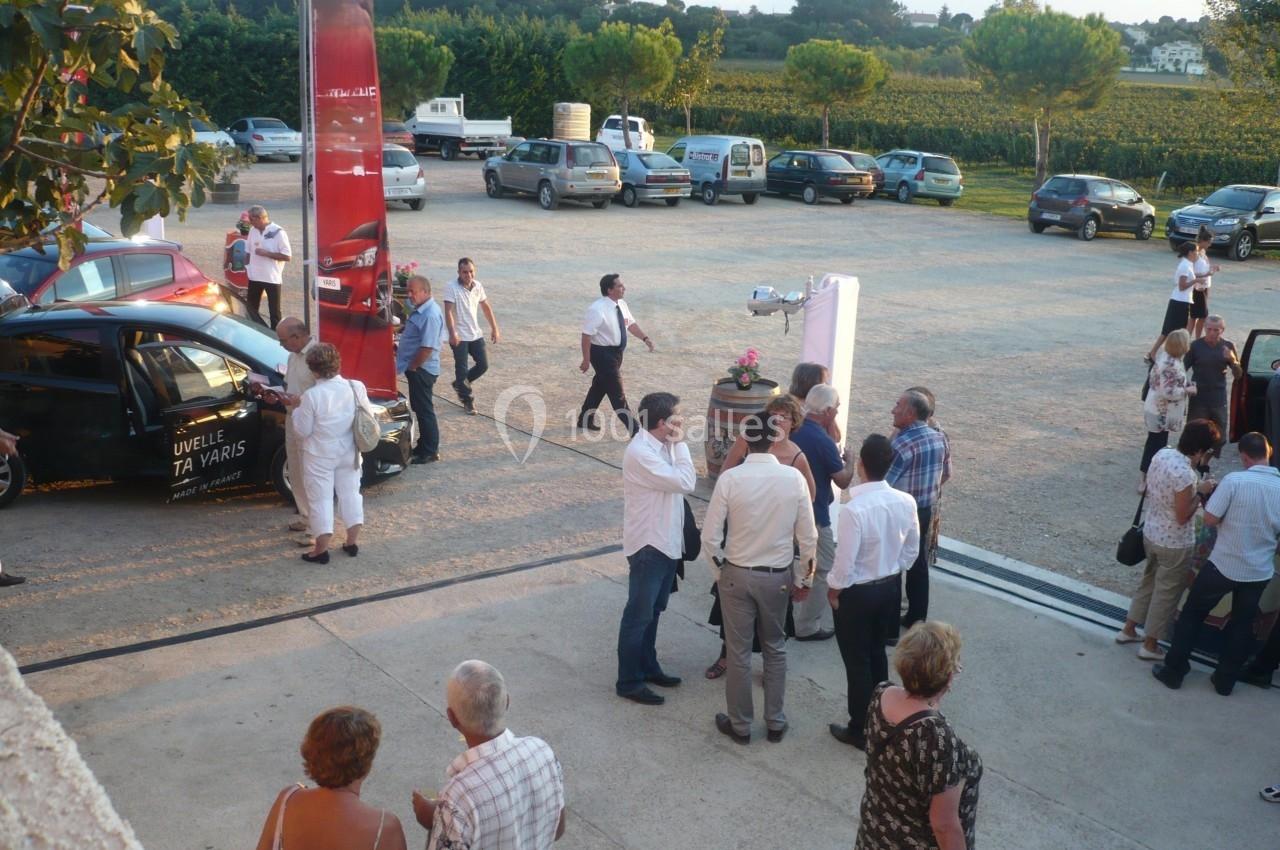Groupe de personnes discutant en extérieur sur un parking, avec des voitures et un paysage rural en arrière-plan.