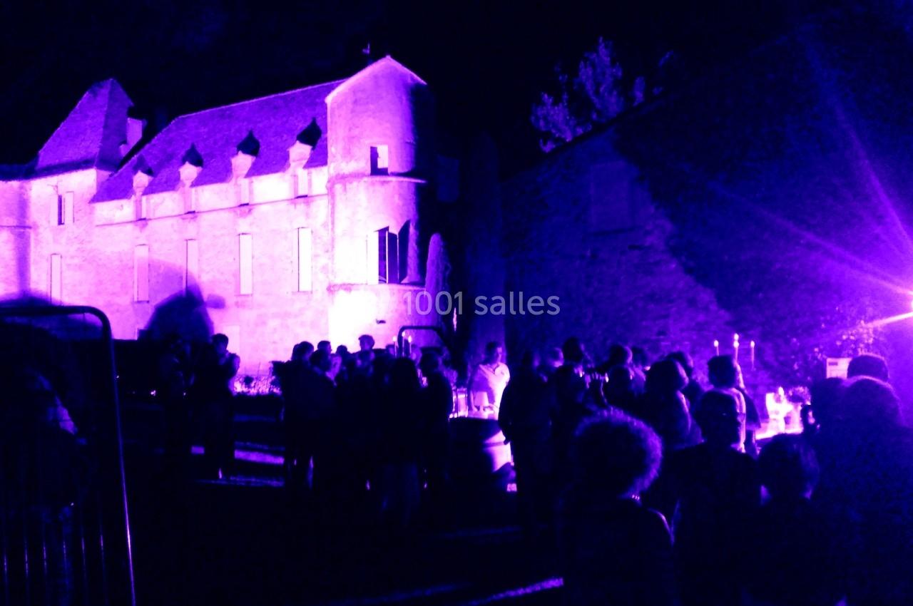 Groupe de personnes rassemblées de nuit devant un bâtiment ancien éclairé par des lumières violettes.