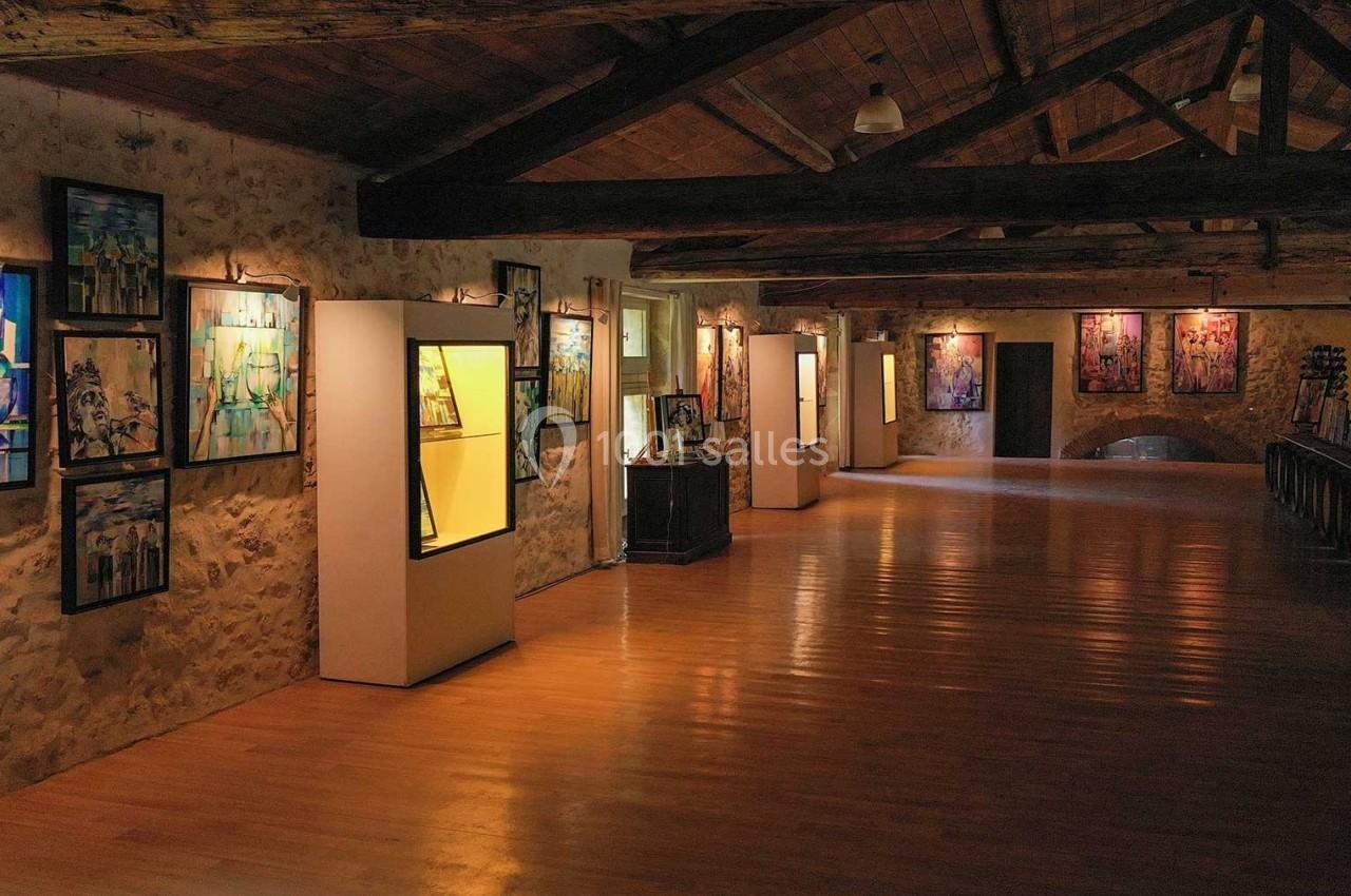 Salle d'exposition avec des œuvres d'art accrochées aux murs en pierre et éclairées par des spots lumineux.