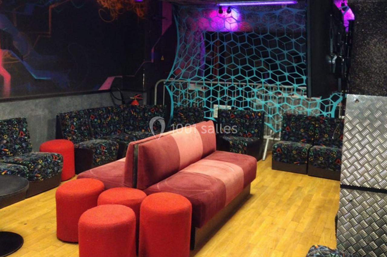 Salle avec canapés colorés, poufs rouges, décorations murales géométriques et éclairage tamisé.