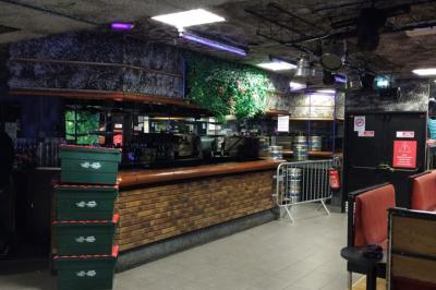 Salle vide avec un sol en carrelage gris foncé, des murs clairs et des portes rouges visibles en arrière-plan.