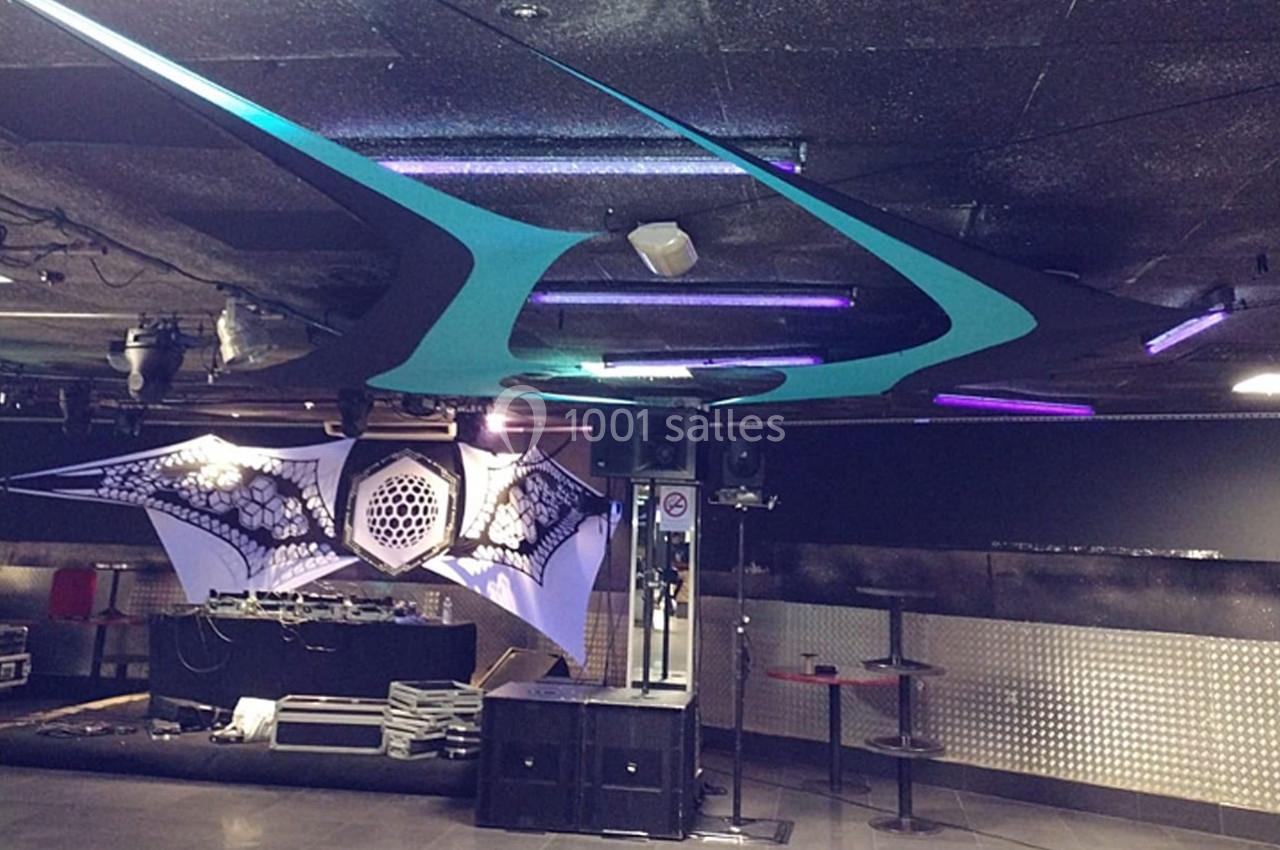 Salle de concert avec scène équipée de matériel audio, décorations lumineuses et plafond aux motifs futuristes.