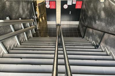 Salle vide avec un sol en carrelage gris foncé, des murs clairs et des portes rouges visibles en arrière-plan.