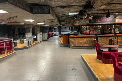 Salle vide avec un sol en carrelage gris foncé, des murs clairs et des portes rouges visibles en arrière-plan.