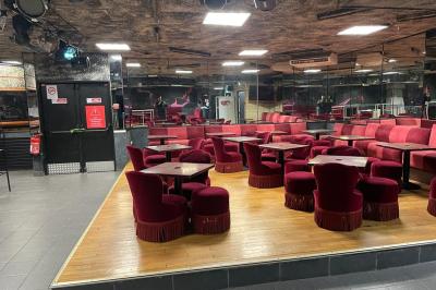 Salle vide avec un sol en carrelage gris foncé, des murs clairs et des portes rouges visibles en arrière-plan.