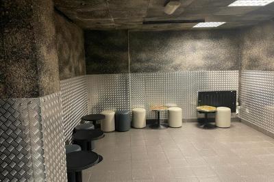 Salle vide avec un sol en carrelage gris foncé, des murs clairs et des portes rouges visibles en arrière-plan.