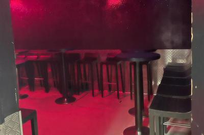 Salle vide avec un sol en carrelage gris foncé, des murs clairs et des portes rouges visibles en arrière-plan.