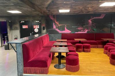 Salle vide avec un sol en carrelage gris foncé, des murs clairs et des portes rouges visibles en arrière-plan.