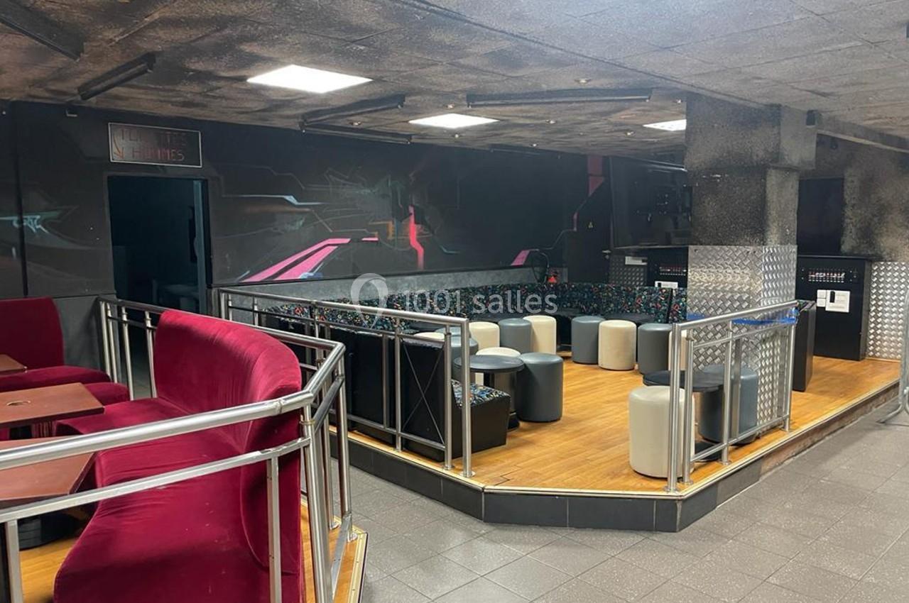 Espace intérieur avec banquettes colorées, tabourets et tables, éclairage artificiel et murs sombres décorés.