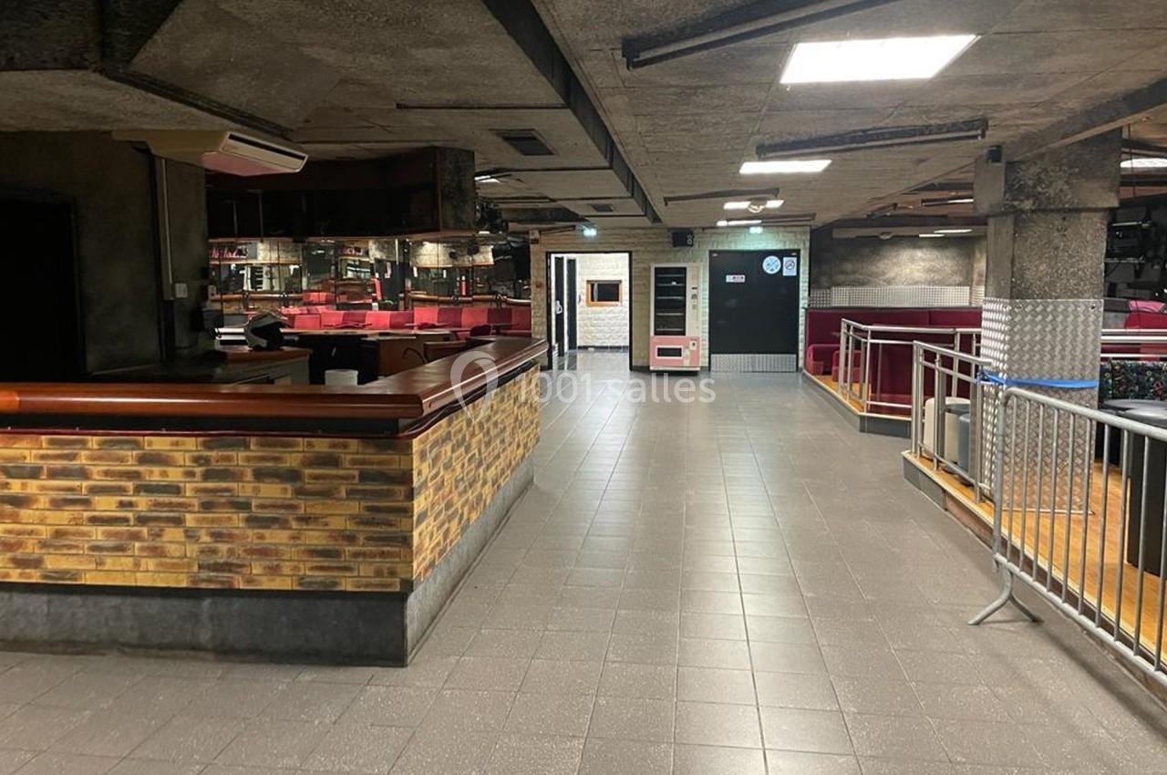 Intérieur d'un espace avec comptoir en briques, sol carrelé, éclairage au plafond et mobilier rouge en arrière-plan.