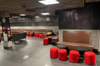 Salle vide avec un sol en carrelage gris foncé, des murs clairs et des portes rouges visibles en arrière-plan.