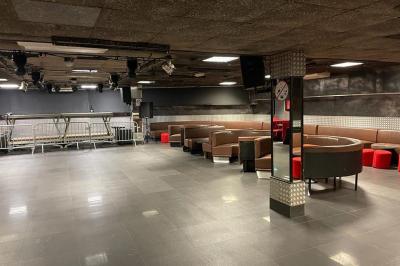 Salle vide avec un sol en carrelage gris foncé, des murs clairs et des portes rouges visibles en arrière-plan.