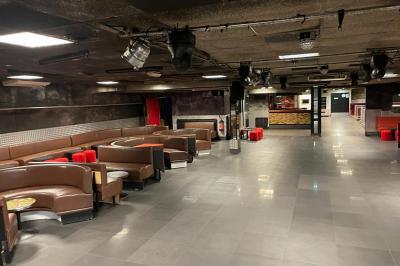 Salle vide avec un sol en carrelage gris foncé, des murs clairs et des portes rouges visibles en arrière-plan.