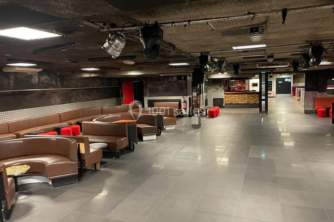 Salle vide avec banquettes en cuir, tables basses, éclairage tamisé et espace central dégagé.