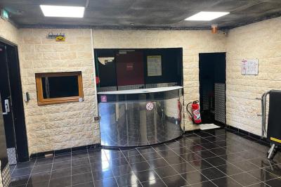 Salle vide avec un sol en carrelage gris foncé, des murs clairs et des portes rouges visibles en arrière-plan.