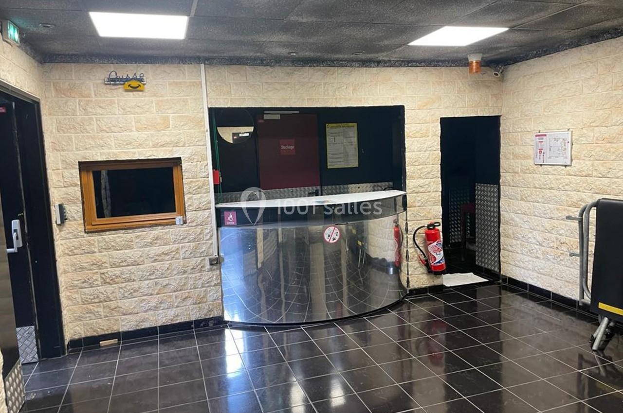 Accueil avec comptoir métallique, murs en pierre claire, sol en carrelage noir et équipements de sécurité visibles.