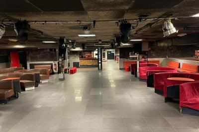 Salle vide avec un sol en carrelage gris foncé, des murs clairs et des portes rouges visibles en arrière-plan.