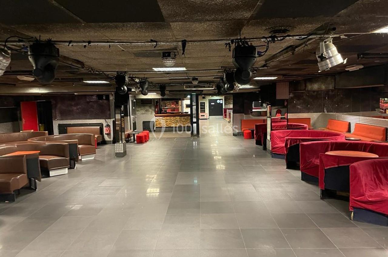 Salle vide avec banquettes rouges et marron, sol en carrelage gris, éclairage tamisé et plafond sombre.