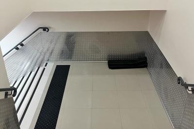 Salle vide avec un sol en carrelage gris foncé, des murs clairs et des portes rouges visibles en arrière-plan.