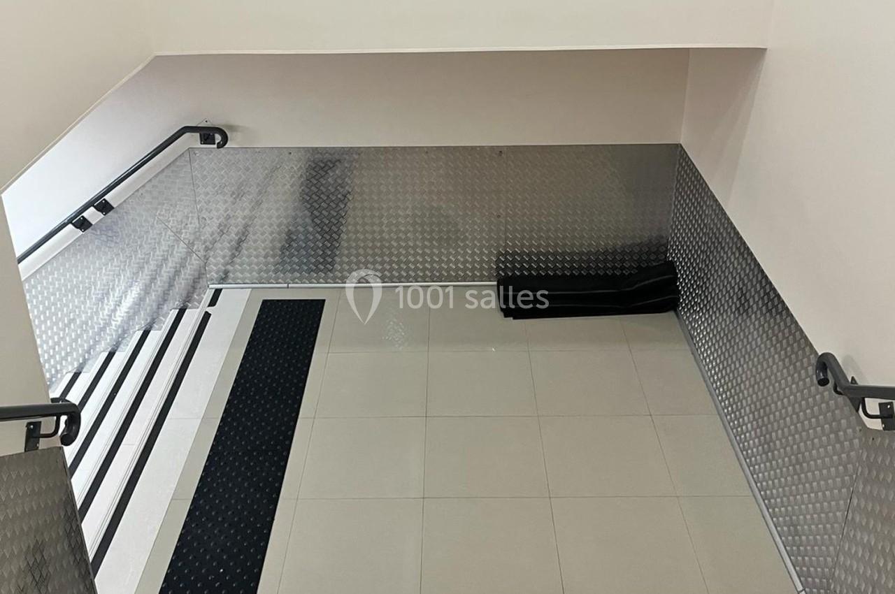 Escalier intérieur avec marches noires antidérapantes et murs recouverts de plaques métalliques texturées.
