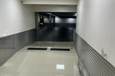 Salle vide avec un sol en carrelage gris foncé, des murs clairs et des portes rouges visibles en arrière-plan.