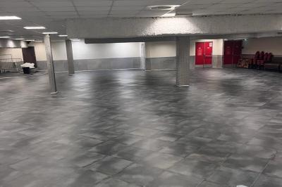 Salle vide avec un sol en carrelage gris foncé, des murs clairs et des portes rouges visibles en arrière-plan.