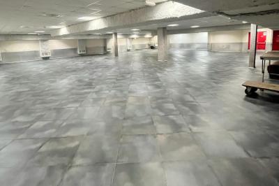 Salle vide avec un sol en carrelage gris foncé, des murs clairs et des portes rouges visibles en arrière-plan.