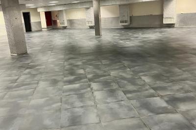 Salle vide avec un sol en carrelage gris foncé, des murs clairs et des portes rouges visibles en arrière-plan.