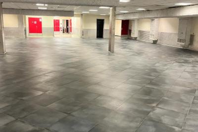 Salle vide avec un sol en carrelage gris foncé, des murs clairs et des portes rouges visibles en arrière-plan.