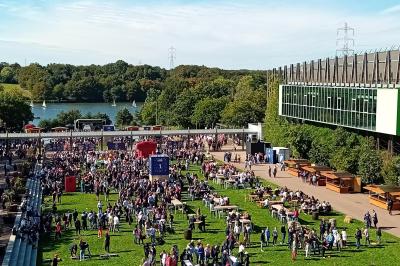 Bâtiment moderne avec façade vitrée, éclairé au crépuscule, reflété dans un plan d'eau calme.