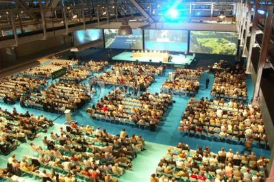 Bâtiment moderne avec façade vitrée, éclairé au crépuscule, reflété dans un plan d'eau calme.