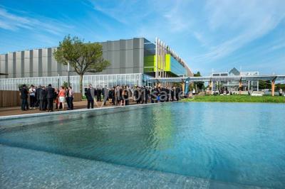 Bâtiment moderne avec façade vitrée, éclairé au crépuscule, reflété dans un plan d'eau calme.