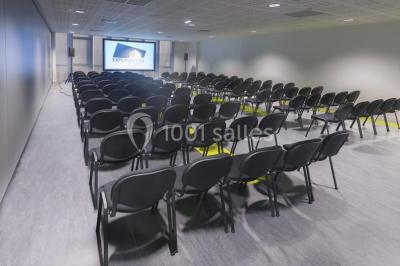 Bâtiment moderne avec façade vitrée, éclairé au crépuscule, reflété dans un plan d'eau calme.