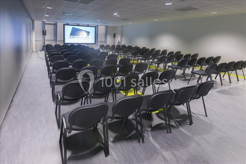 Salle de conférence vide avec des rangées de chaises noires orientées vers un écran de projection allumé.